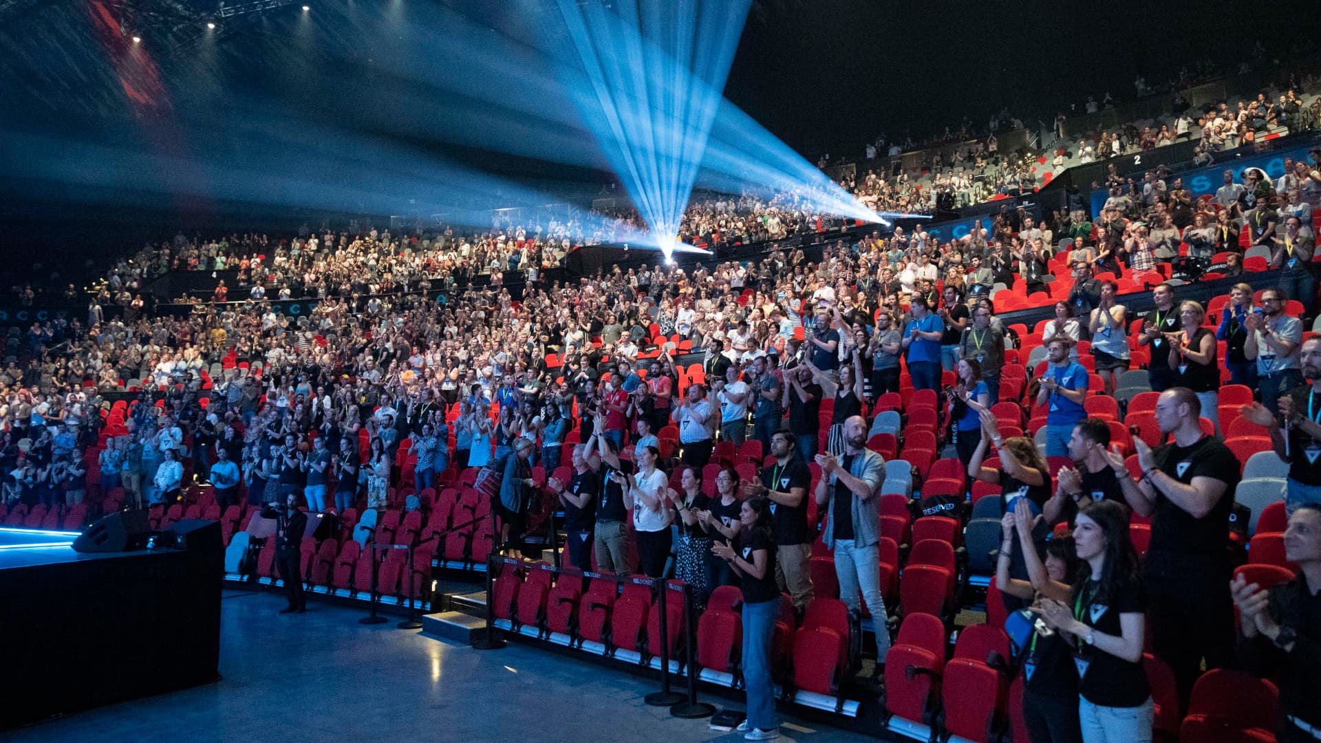 Delegates standing and applauding in a packed arena at a conference